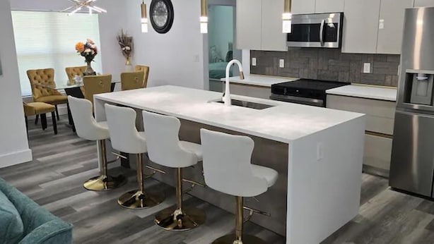 Een moderne keuken met een centraal eiland, barstoelen, roestvrijstalen apparatuur en een eetgedeelte met een ronde tafel en stoelen.