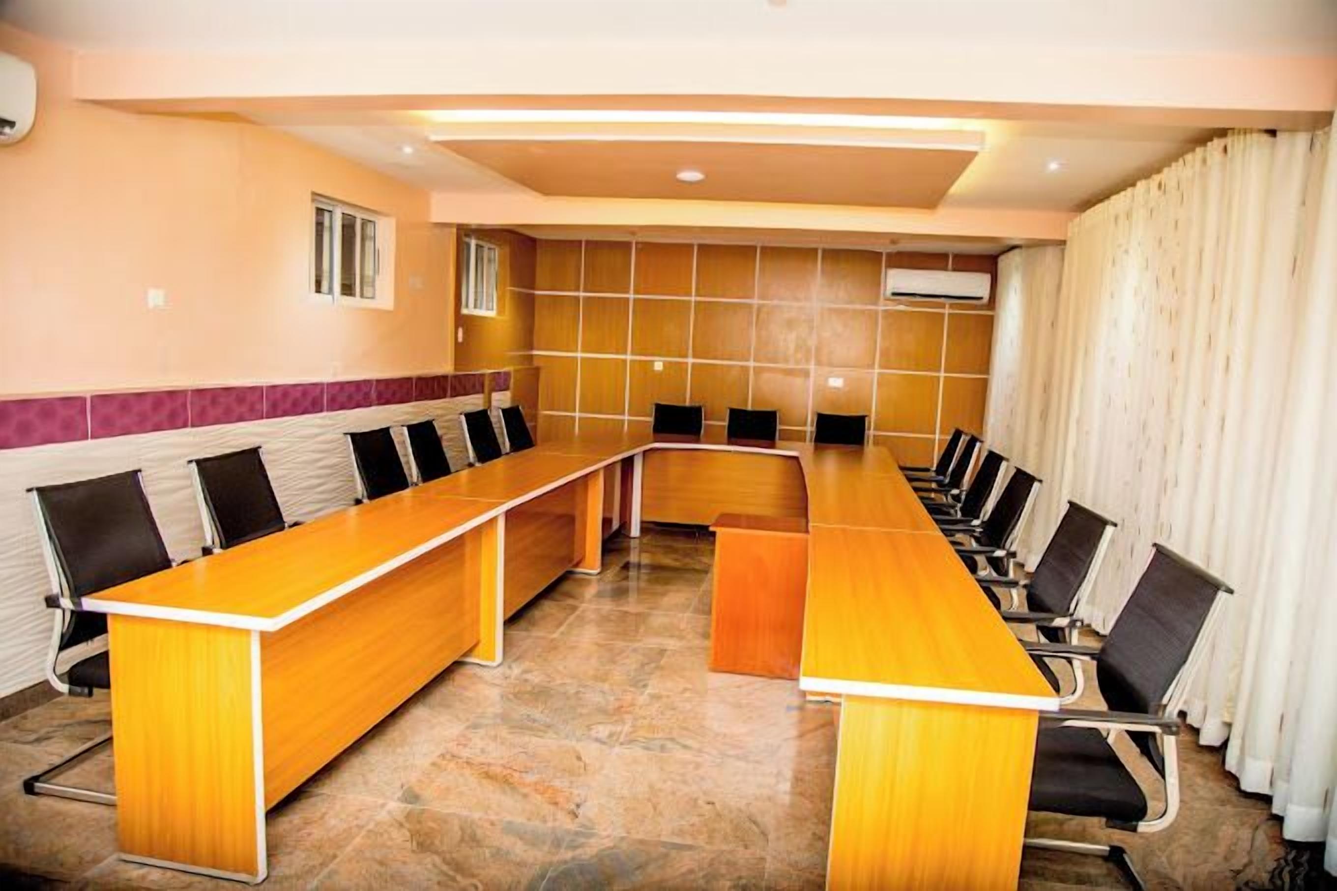 A conference room with a long wooden table, black chairs, and a tiled floor.