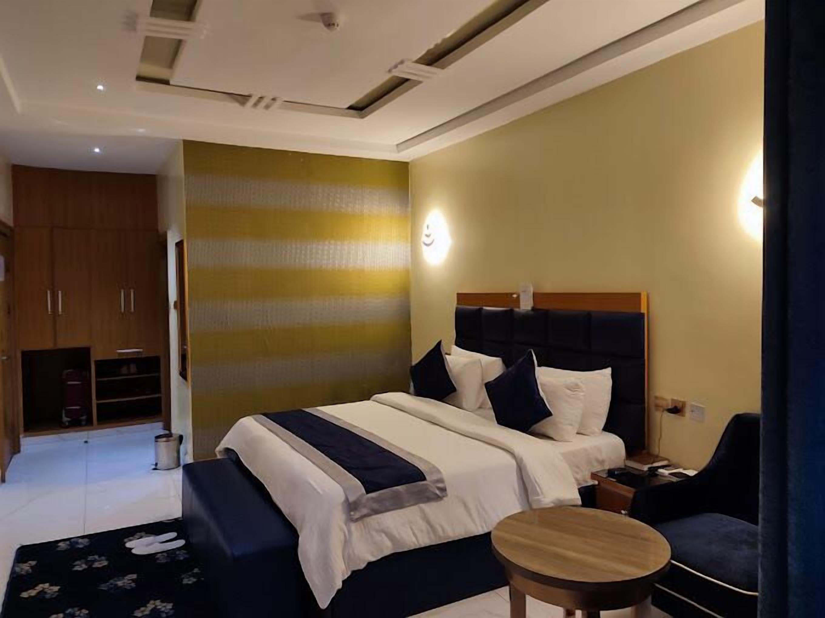 Une chambre d’hôtel avec un lit, une table de chevet et une petite table ronde. On y trouve également une armoire et une poubelle dans un coin.