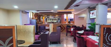 A restaurant with a bar area, cushioned booths, and red tablecloths.