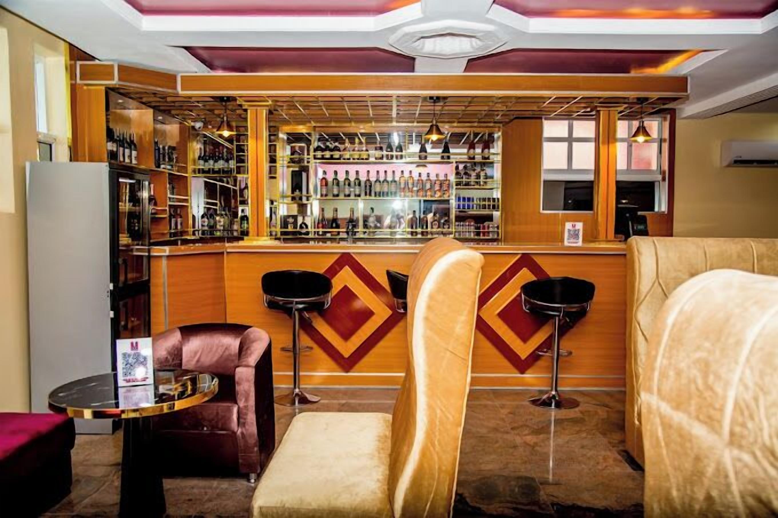 A bar area with a wooden bar counter, shelves of bottles, and two bar stools.