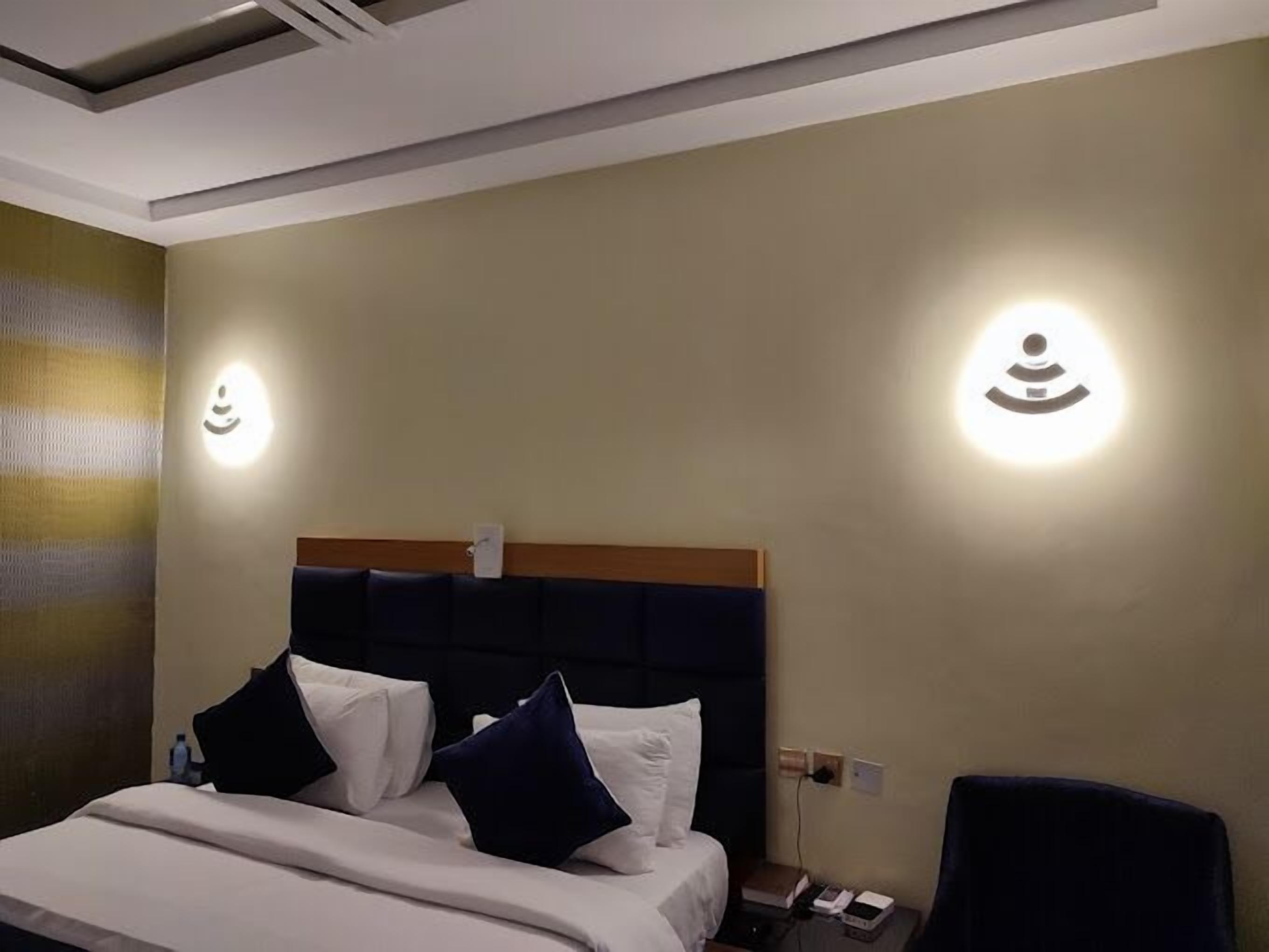 A hotel room with a bed, a nightstand, and two wall-mounted light fixtures.