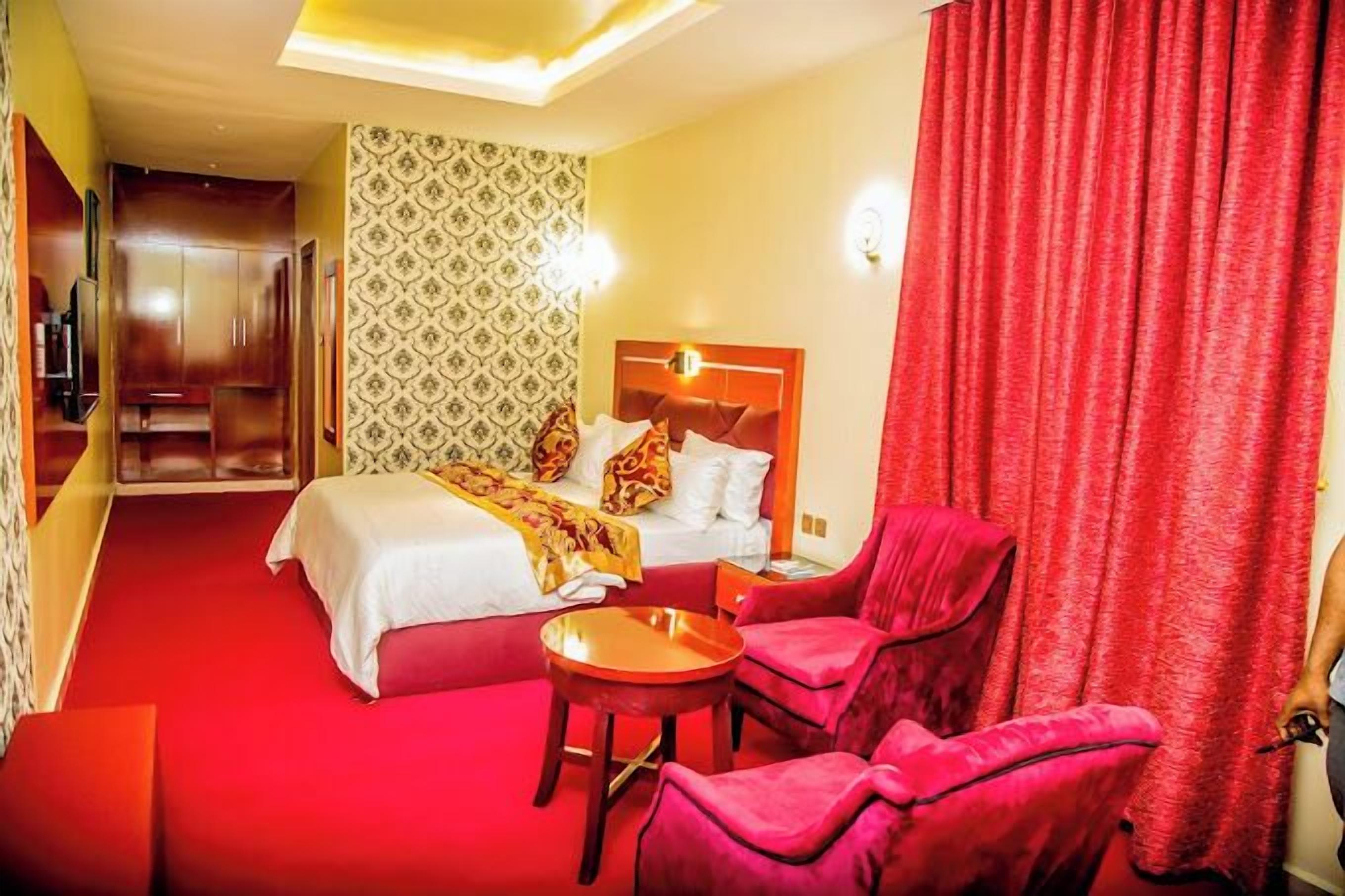 A hotel room with a bed, two red armchairs, a small table, and a red curtain.