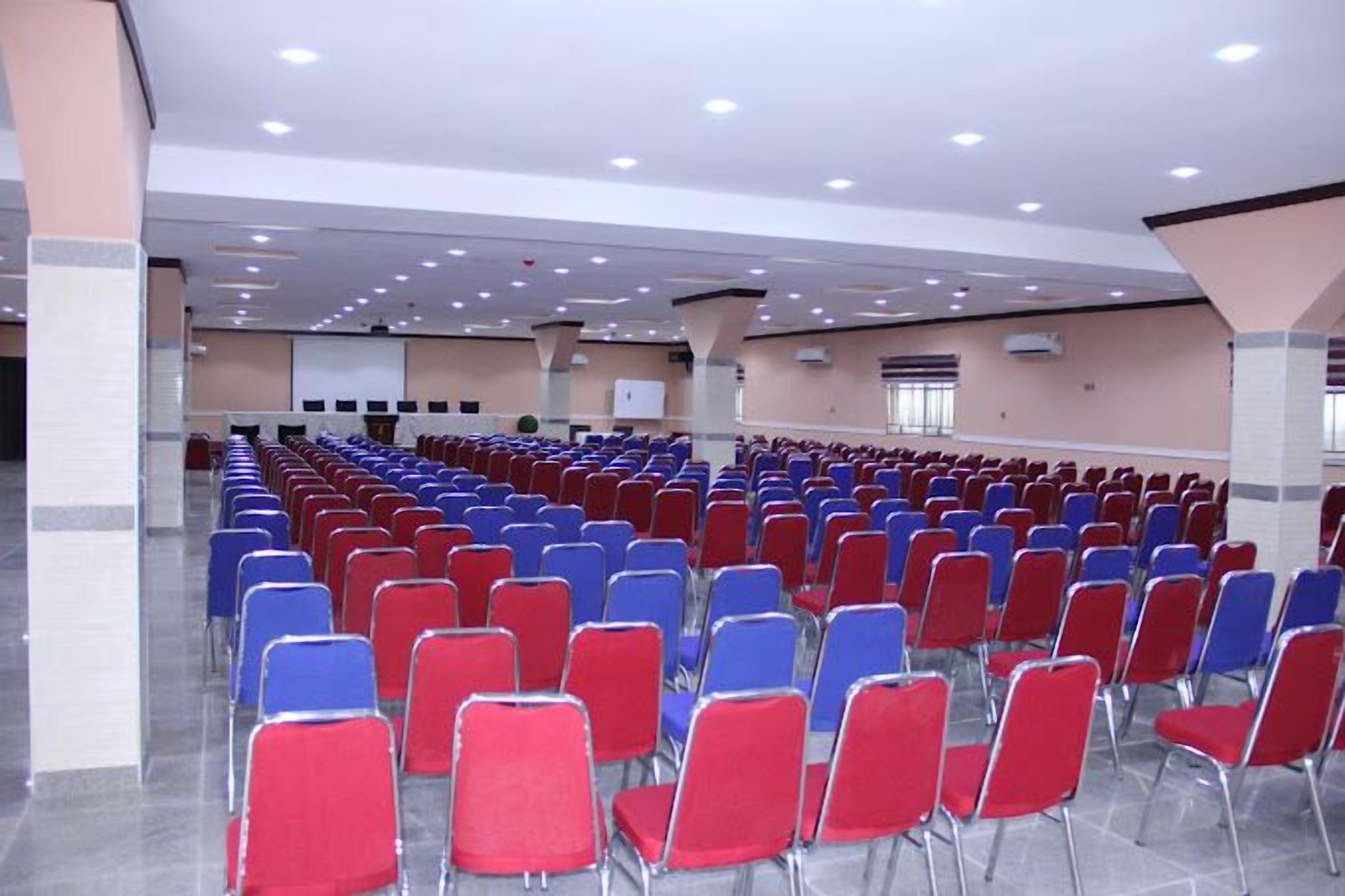 Um salão amplo com fileiras de cadeiras vermelhas e azuis, dispostas para um evento.