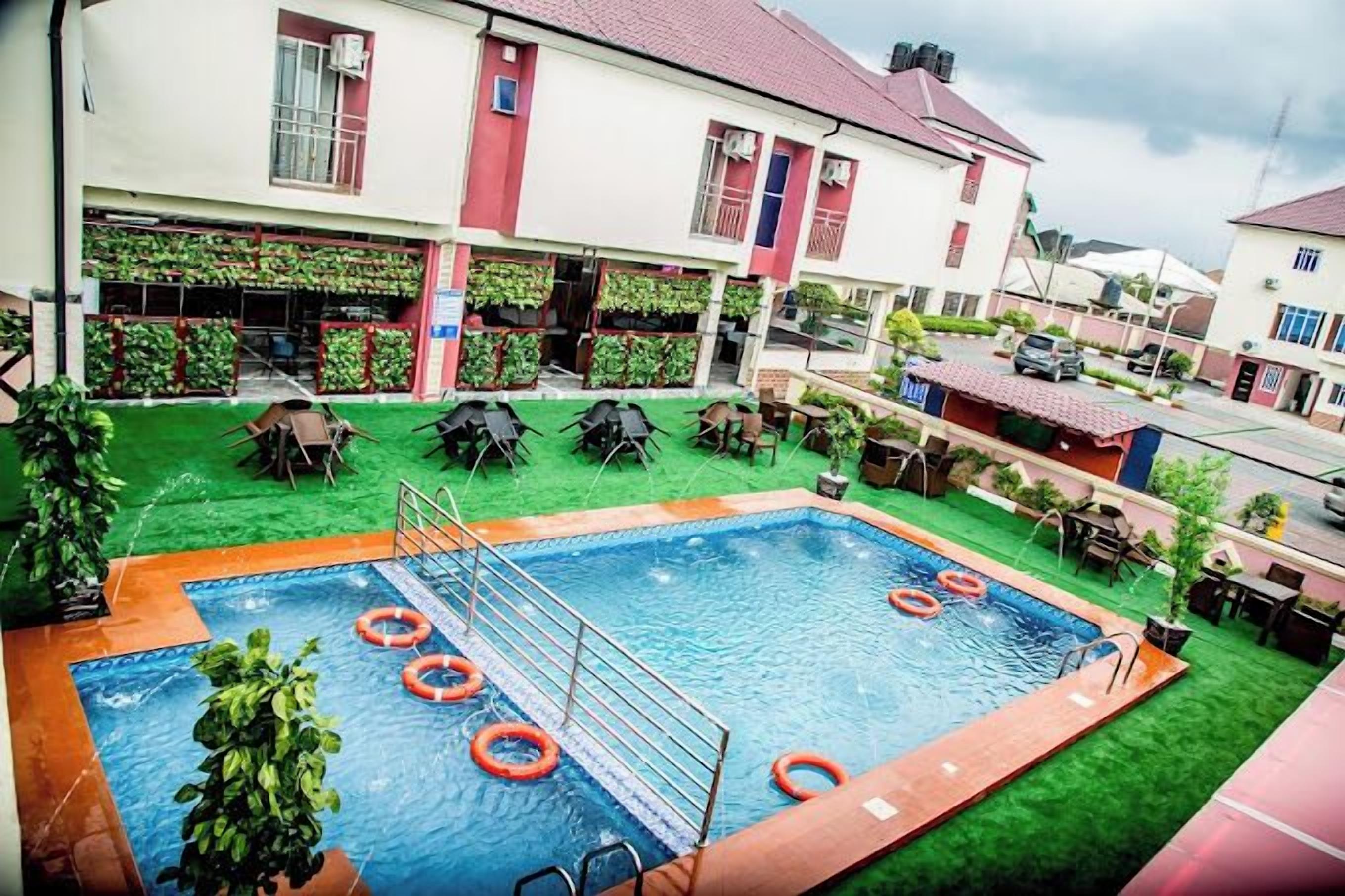 A swimming pool with a diving board, surrounded by green artificial grass and outdoor seating.