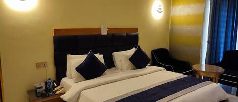 Ein Hotelzimmer mit einem großen Bett, einem Nachttisch, einem Sessel und einem kleinen Tisch.