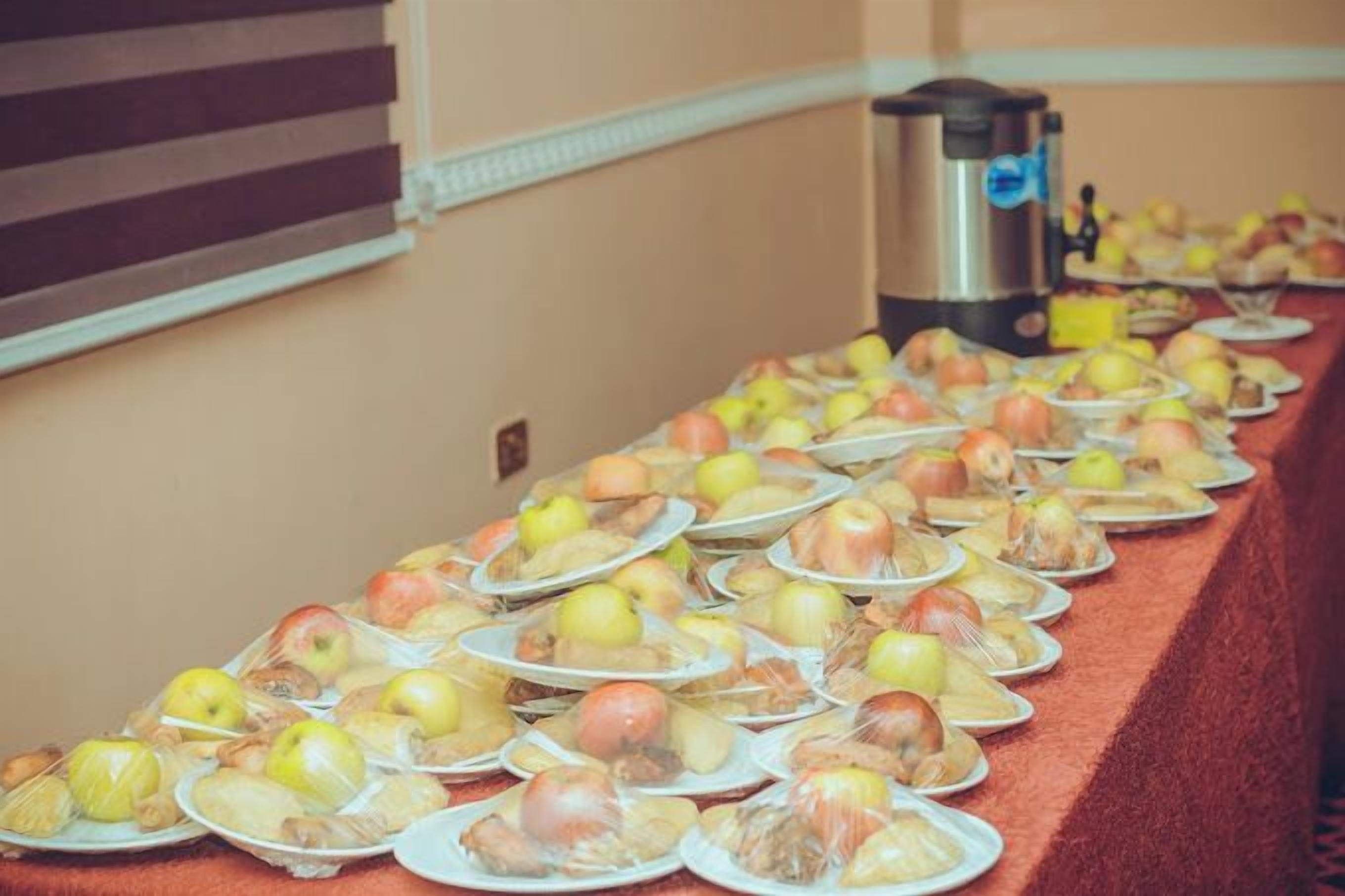A buffet table with plates of food, including apples and other items, in a room with a red carpet and a coffee maker in the background.