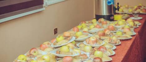 A buffet table with plates of food, including apples and other items, in a room with a red carpet and a coffee maker in the background.