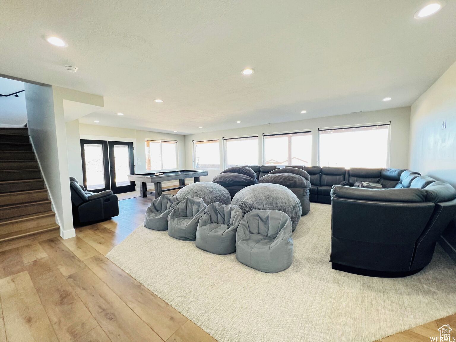 A spacious living room with a pool table, grey bean bag chairs, a black sofa, and a staircase.