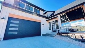 A modern two-story house with a large garage, a covered patio, and a view of the surrounding landscape. - Bear Lake getaway for the whole family! Sleeps 32! Beach access included!! (Garden City)