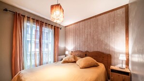 Ein Schlafzimmer mit einem hölzernen Kopfteil, einem großen Bett mit zwei Kissen, einem Nachttisch mit einer Lampe und einem Fenster mit Vorhängen.