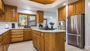 A modern kitchen with wooden cabinets, a stainless steel refrigerator, and a large island. - Summit Sanctuary: Urban Elegance mins from Downtown (Flagstaff)