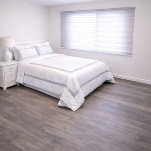 A bedroom with a bed, a nightstand, a lamp, and a window with blinds.