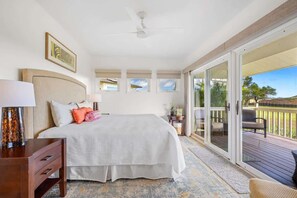 A bedroom with a large bed, a nightstand, a desk, and a sliding glass door leading to a balcony.