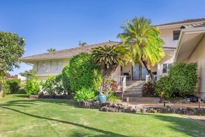 A two-story house with a well-maintained lawn, a stone pathway, and a variety of tropical plants.