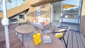 Un patio al aire libre con una mesa redonda, sillas, un sofá y un cerramiento de vidrio que da a un balcón.