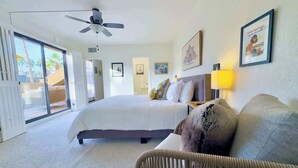 Habitación de hotel con cama, una silla, ventilador de techo y un ventanal grande.