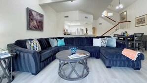 Una sala de estar moderna con un sofá modular, una mesa de centro redonda y una escalera que sube a un nivel superior.