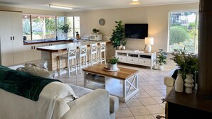 A modern living room with a kitchen area, a dining table, and a TV mounted on the wall. - Beautiful Ocean Views , Internet & Smart TV (Guilderton)
