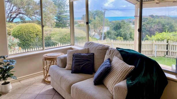 A conservatory with a beige sofa, a small round table, and a potted plant. - Beautiful Ocean Views , Internet & Smart TV (Guilderton)