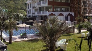 Un hotel con un café en la azotea y música en vivo, rodeado de exuberante vegetación y una zona de piscina.