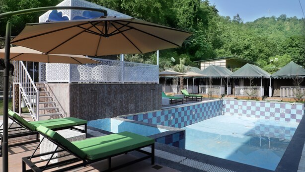 Una piscina con sillas de descanso y sombrillas, rodeada por una valla blanca y follaje.