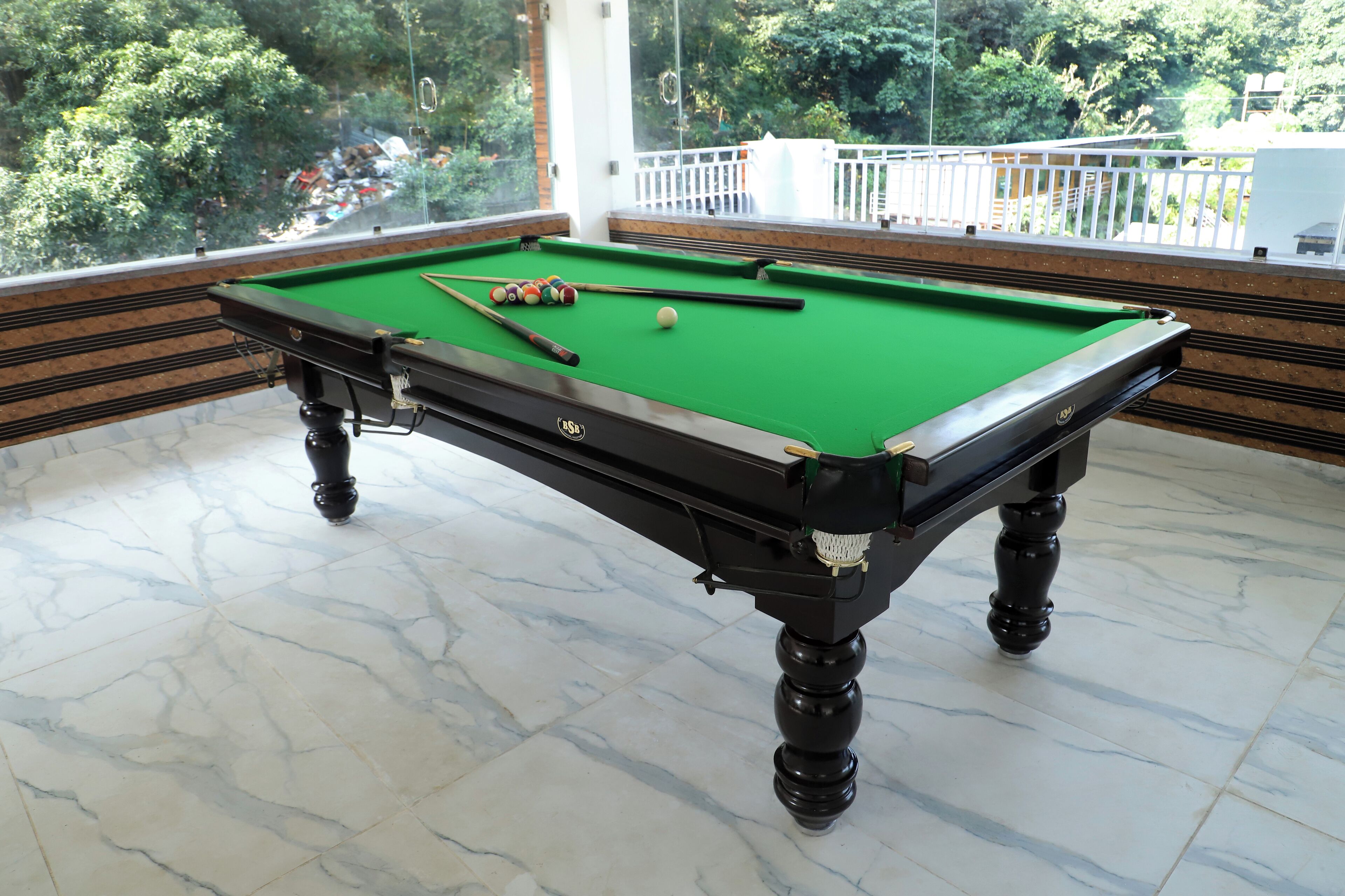 A pool table with a green felt surface, surrounded by a white marble floor.