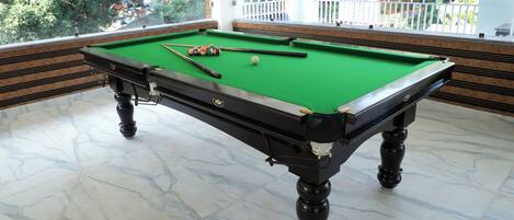 A pool table with a green felt surface, surrounded by a white marble floor.