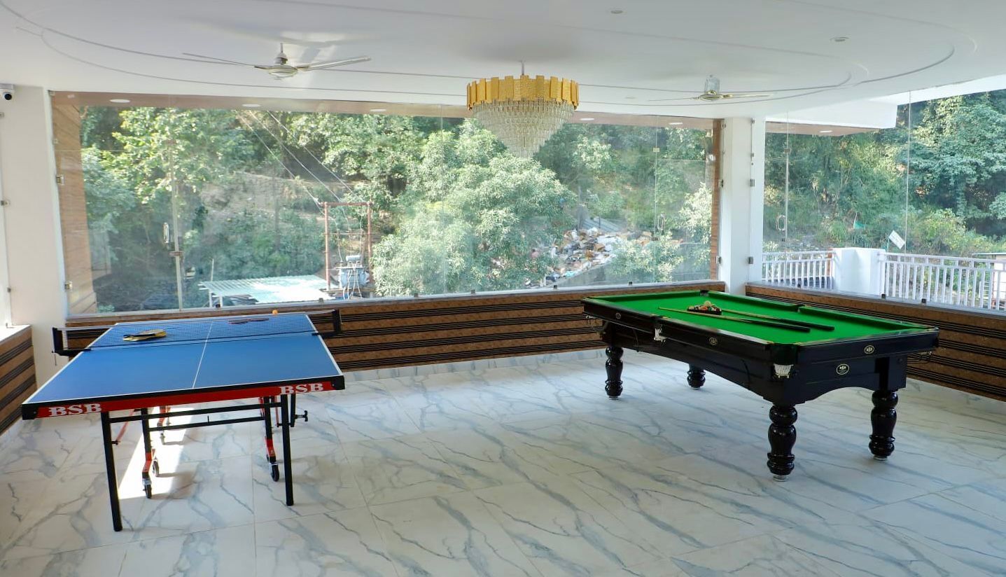 A pool table and ping pong table in a room with large windows overlooking a forested area.