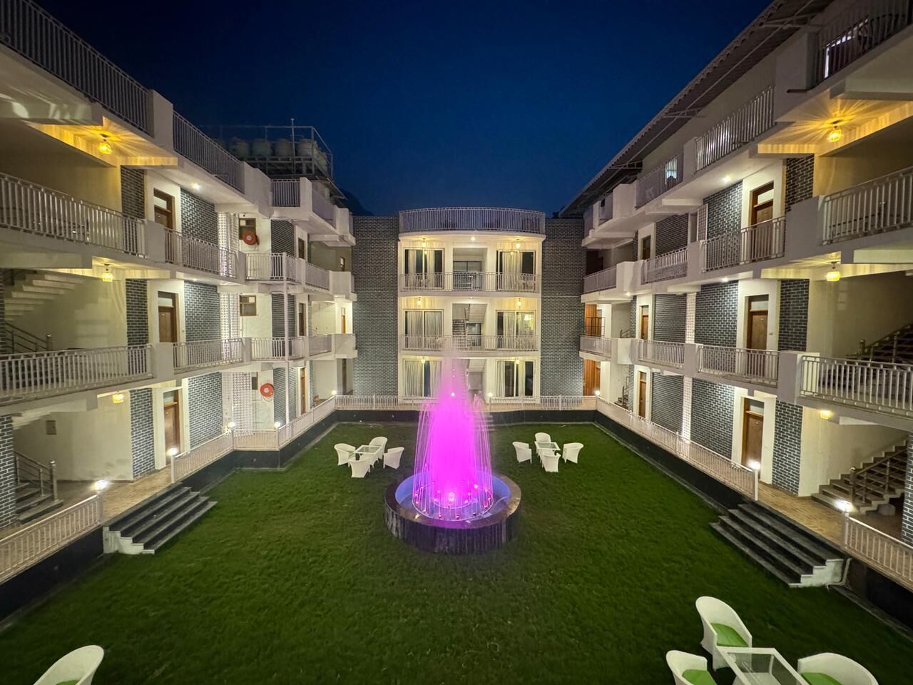 Un hotel de varios pisos con un patio central que tiene una fuente, asientos al aire libre y un césped bien cuidado.