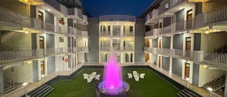 Un hotel de varios pisos con un patio central que tiene una fuente, asientos al aire libre y un césped bien cuidado.