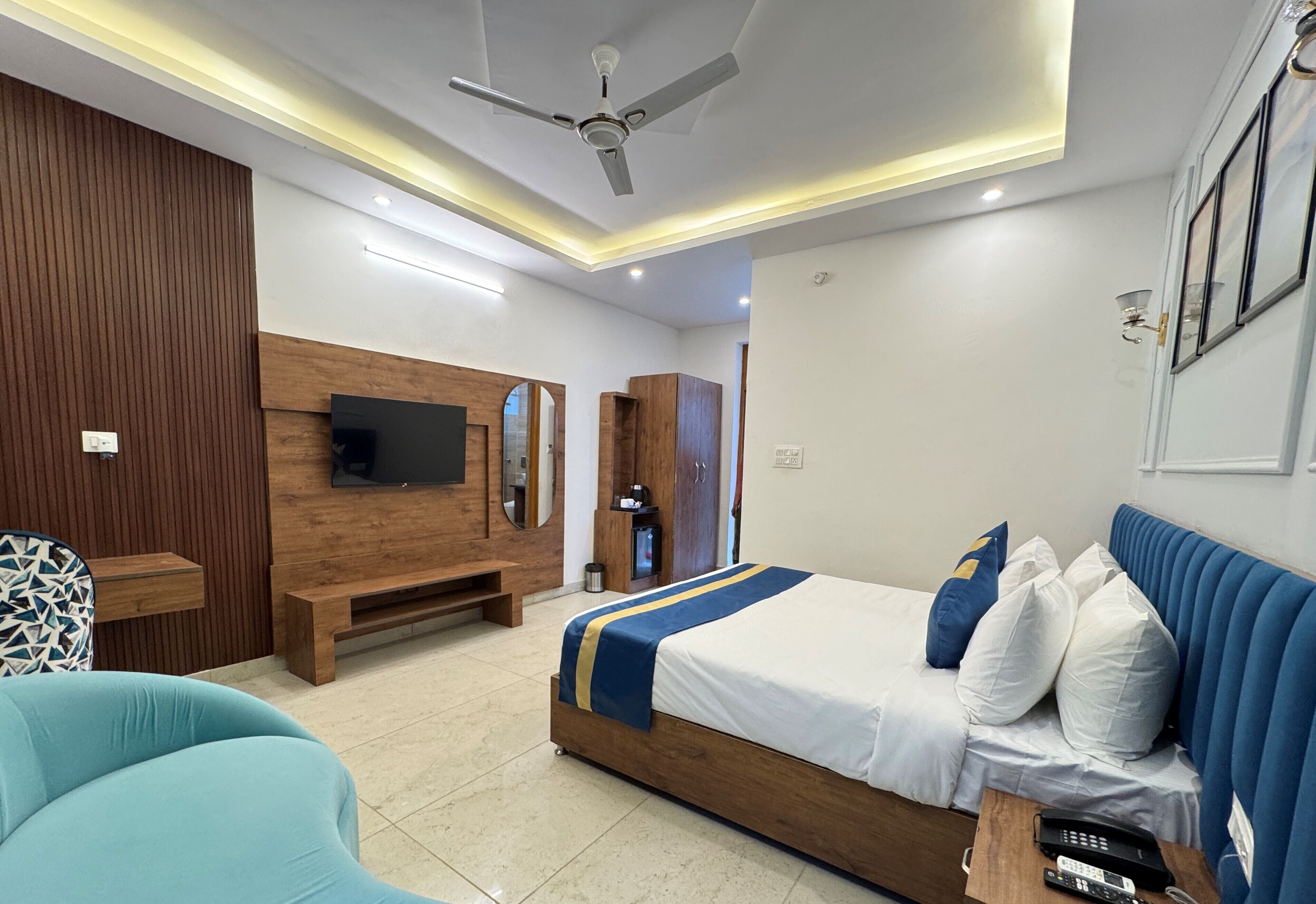 A modern hotel room with a wooden bed, a TV mounted on the wall, a ceiling fan, and a bench.