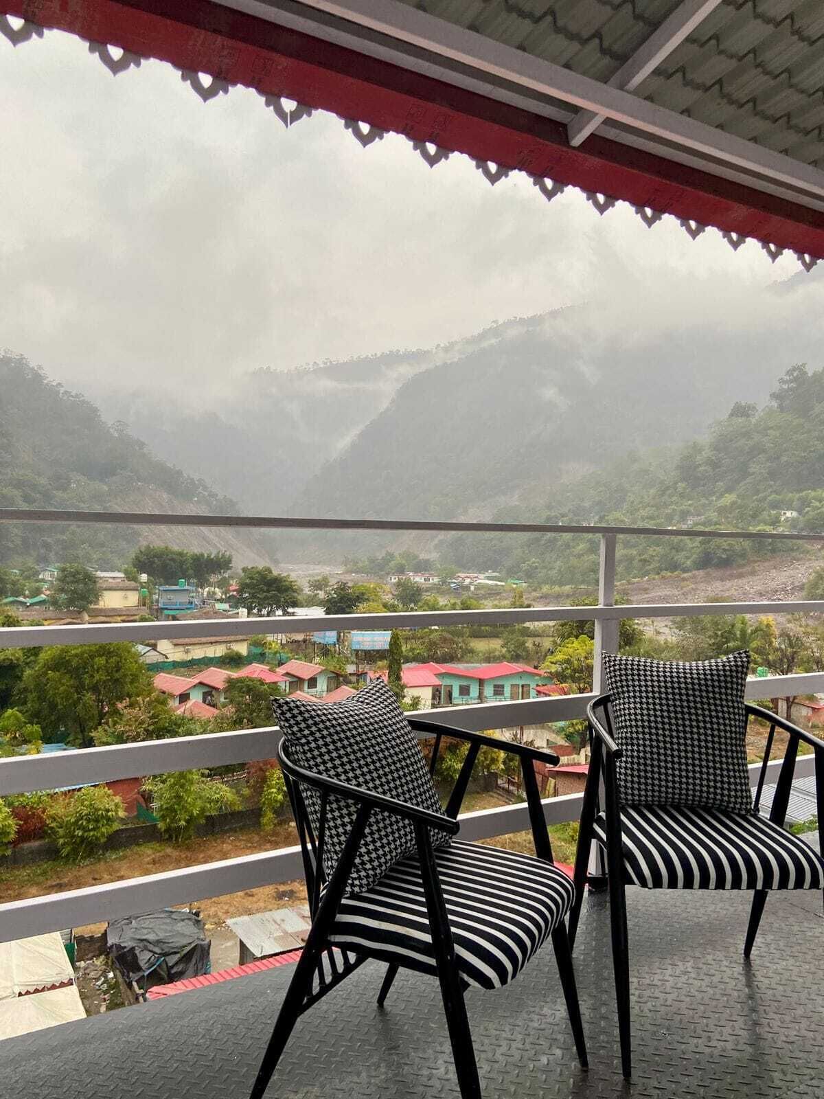 A balcony with two chairs and a view of a valley with houses and greenery.