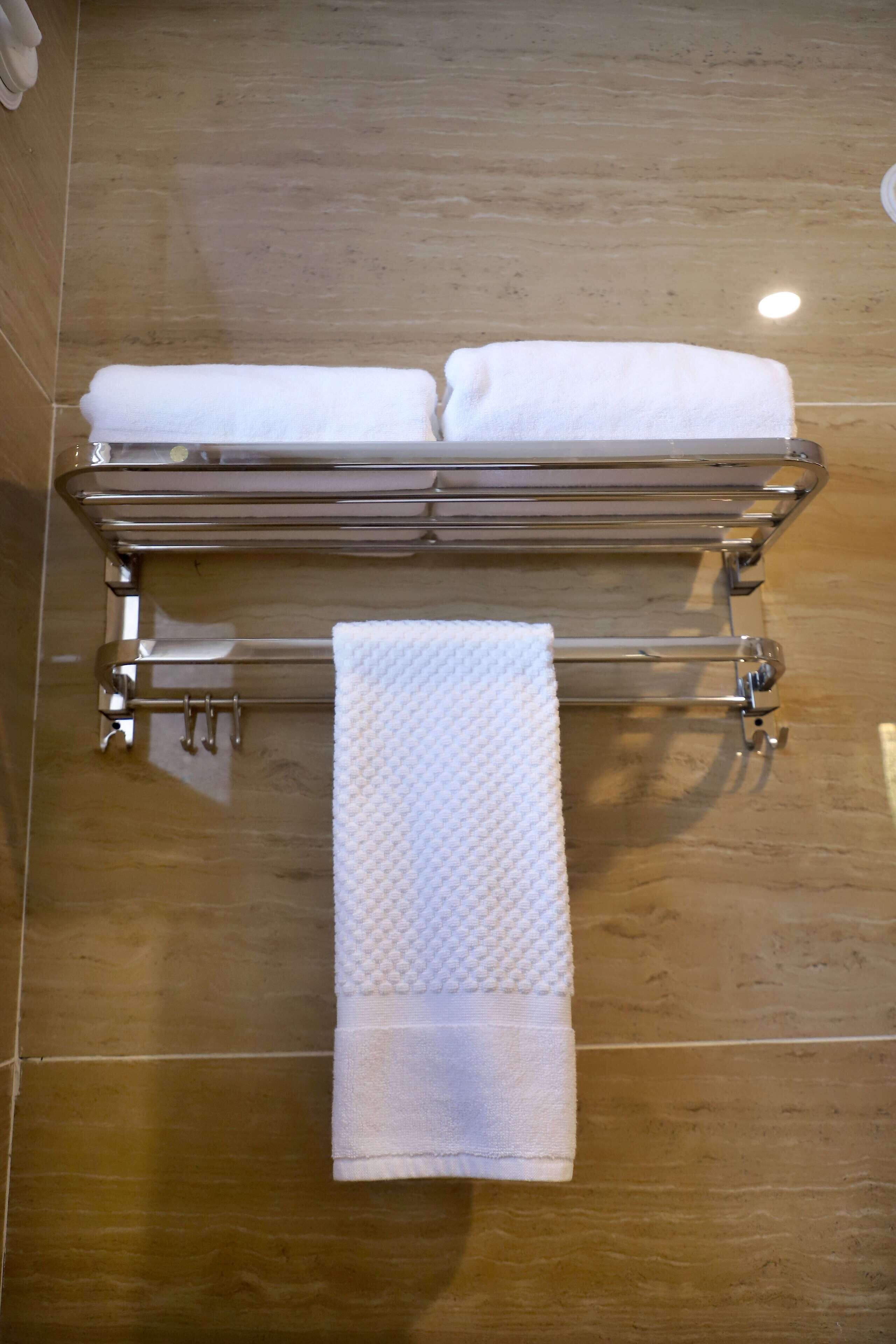 A bathroom with a towel rack holding two neatly folded white towels and a single towel hanging below.