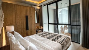 Una habitación de hotel moderna con una cama grande, paneles de madera, un escritorio y un ventanal con cortinas.
