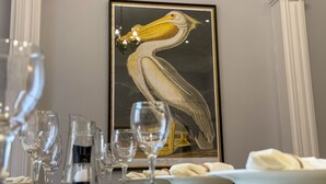 A framed artwork of a pelican on a wall, a chandelier, and a table with wine glasses and plates. - Egerton House Penrith -  a cottage that sleeps 8 guests in 4 bedrooms (Penrith)