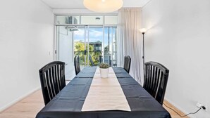 Un comedor moderno con una mesa larga, sillas negras, una planta en maceta y vistas al exterior a través de puertas de cristal.