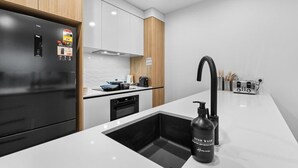 A modern kitchen with a black refrigerator, white cabinets, and a black sink with a soap dispenser.