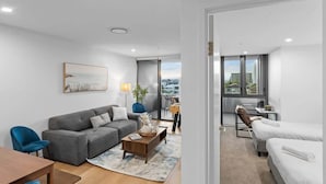 Ein modernes, helles Wohnzimmer mit einem grauen Sofa, einem Holztisch und Blick auf die Stadt durch große Fenster.