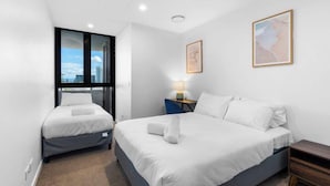Ein Hotelzimmer mit zwei Betten, einem Schreibtisch, einem Stuhl und einem Fenster mit Blick auf die Stadt.