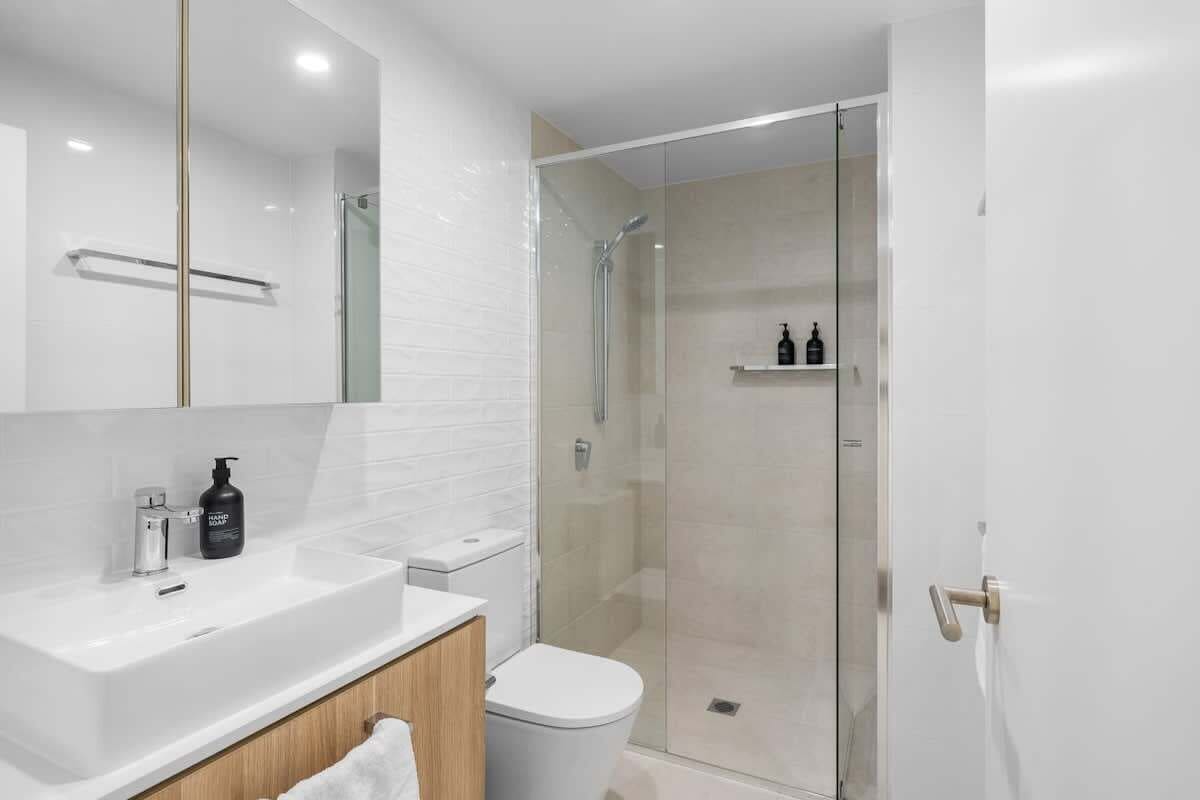Ein modernes Badezimmer mit einer gläsernen Duschkabine, einem weißen Waschbecken und einer Toilette.