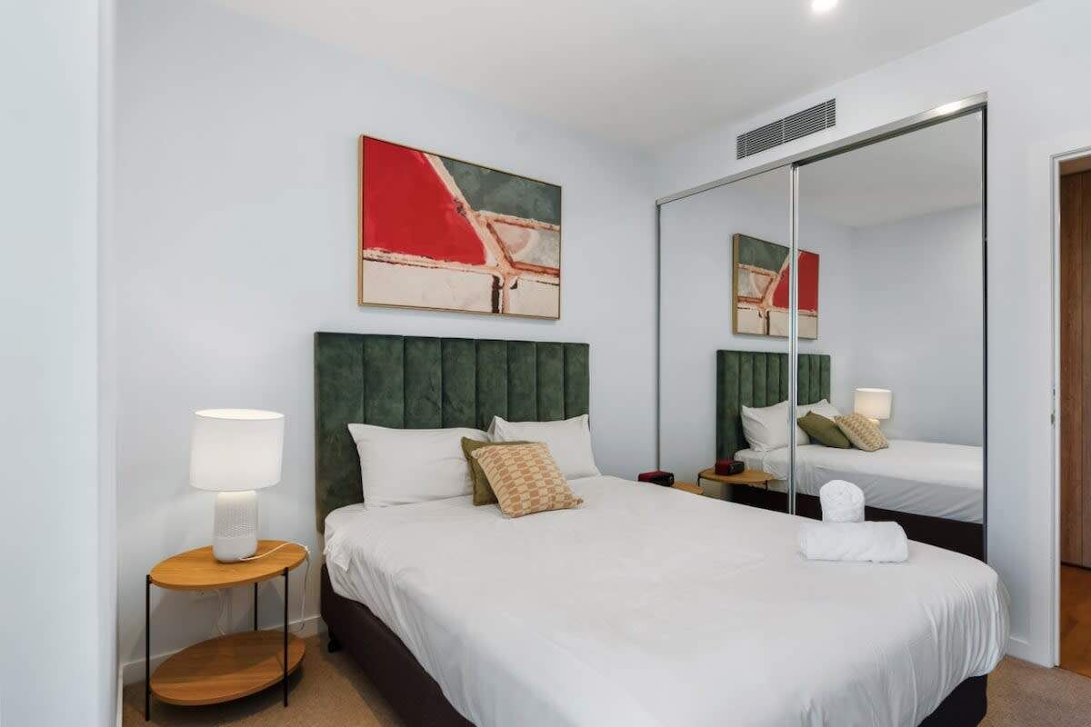 A hotel room with a large bed, a bedside table with a lamp, a mirror, and artwork on the wall.