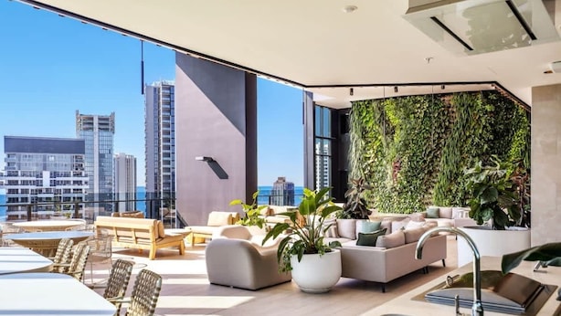 Eine moderne Dachterrasse mit Stadtblick, ausgestattet mit einer großen Innenwand aus Pflanzen, gemütlicher Sitzgelegenheiten und einer integrierten Küchenzeile.
