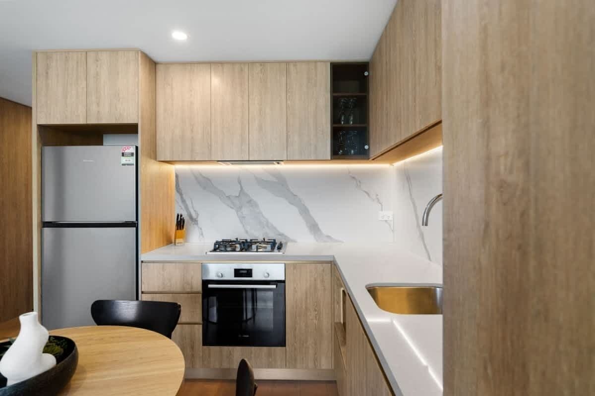 A modern kitchen with wooden cabinets, a marble backsplash, a gas stove, an oven, and a sink.