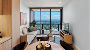 Ein modernes Wohnzimmer mit Sofa, Couchtisch und Fernseher, mit einem großen Fenster und Blick auf die Stadt.
