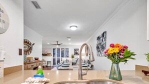 A modern kitchen with a double sink, a vase of flowers, and a dining area in the background.