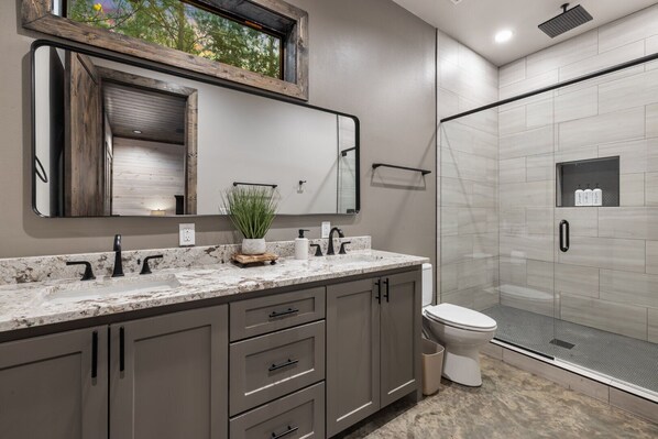 A modern bathroom with a large mirror, a granite countertop, a toilet, and a shower area.