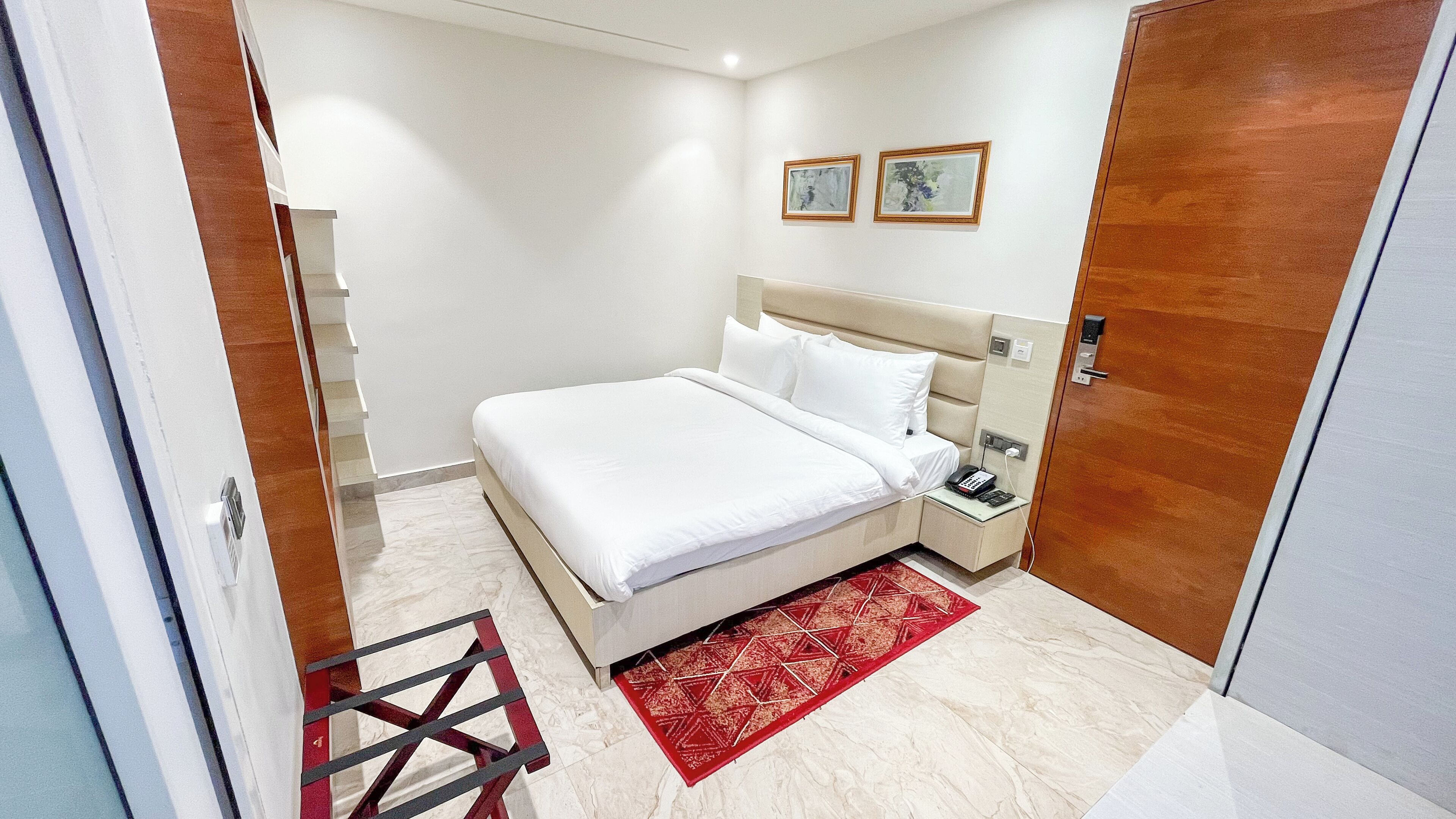 A hotel room with a bed, bedside table, and a red patterned rug.