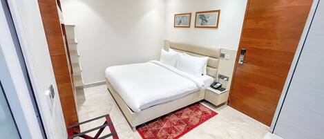 A hotel room with a bed, bedside table, and a red patterned rug.