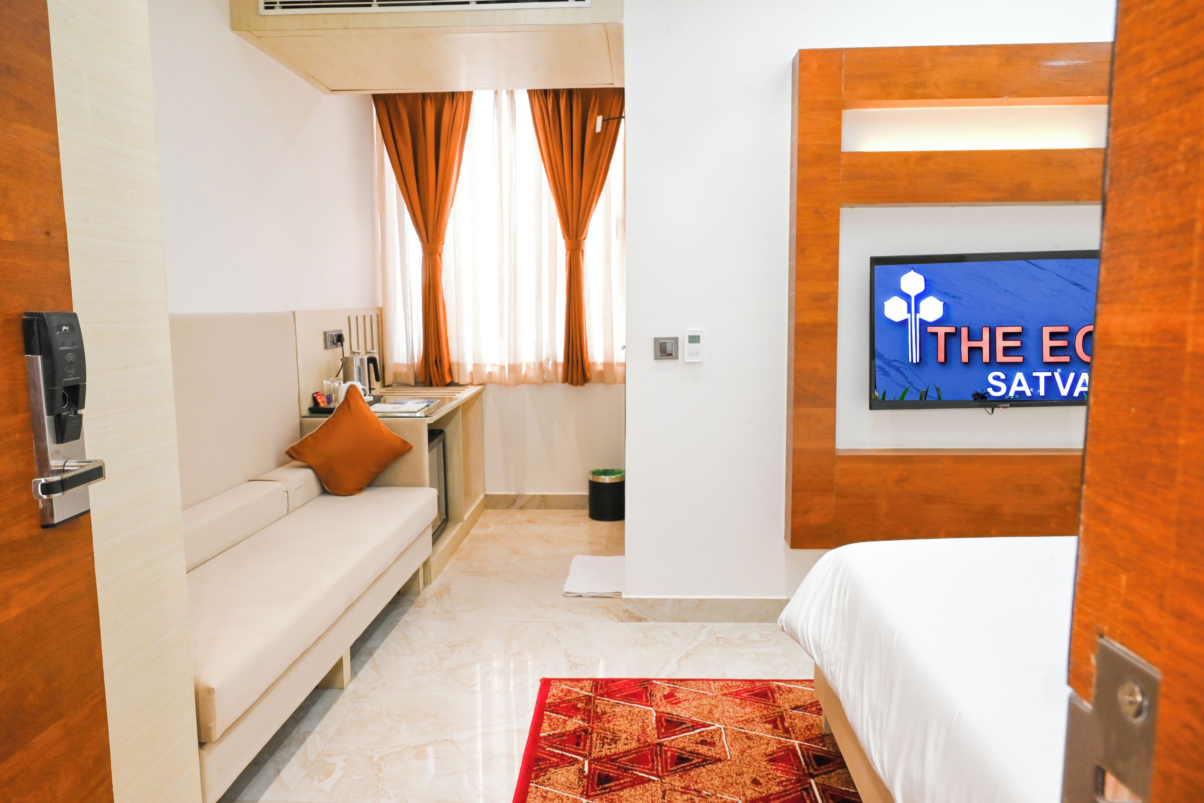 Ein Hotelzimmer mit einer Couch, einem Bett, einem Fernseher, einer kleinen Küchenzeile und einem roten Teppich mit Muster.